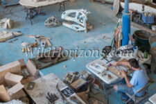 Overhead view of Fossilogic paleo prep lab in Orem, Utah, USA, owned by Brock Sisson. In the foreground, Seth Bourgeous is preparing the pelvis of an Allosaurus fragilis skeleton for casting. Other Allosaurus bones are spread out on the two long tables next to him. In the background Everett Black, on left, wears a half-mask respirator while blowing limestone dust away from a turtle specimen from the Green River Formation of SW Wyoming; and Brock Sisson, on right is welding a support armature for a skeleton. The Allosaurus skeleton is of Jurassic age, from the Morrison Formation, Ten Sleep, Wyoming. Also shown in this photo are replicas of a Majungasaurus atopus dinosaur skull of Cretaceous age from Majunga Basin in Madagascar - the white skull in the black box, lower left corner, and the tan skull on floor in front of Everett Black; a large white skull sculpture with few original parts from a new species of Therapod dinosaur - also on floor in front of Everett Black; a real Wooly Rhino skull, Coelodonta antiquitatis, of Pleistocene age from Siberia - dark brown, on floor in front of Seth Bourgeous; and a replica of a Saber-tooth Cat skull, Smilodon fatalis, of Pleistocene age from Rancho La Brea Tar Pits, Los Angeles, California - on table in front of Seth. Model releases available for all three men.